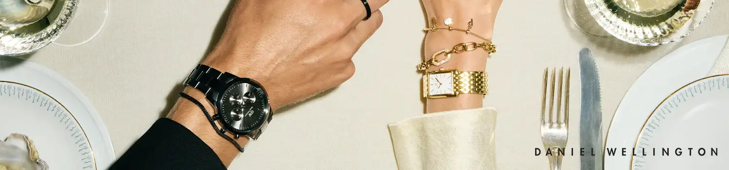 Den här bilden framhäver den tidlösa elegansen och sofistikerade designen som kännetecknar Daniel Wellington-klockor. Till vänster ser vi en stilren herrklocka med ett svart armband och minimalistisk urtavla, medan till höger presenteras en elegant damklocka i gyllene ton med en klassisk kvadratisk urtavla. Bilden fångar en exklusiv middagssituation, vilket speglar märkets fokus på stil och kvalitet, perfekt för både vardag och fest. Daniel Wellington är känt för att kombinera enkelhet med lyx, vilket gör deras klockor till en självklar accessoar för alla tillfällen.